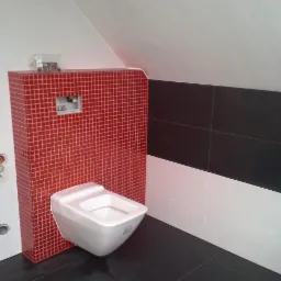 Podwieszana toaleta z zabudową z czerwonej mozaiki w łazience w trakcie remontu, widoczne niedokończone prace elektryczne.