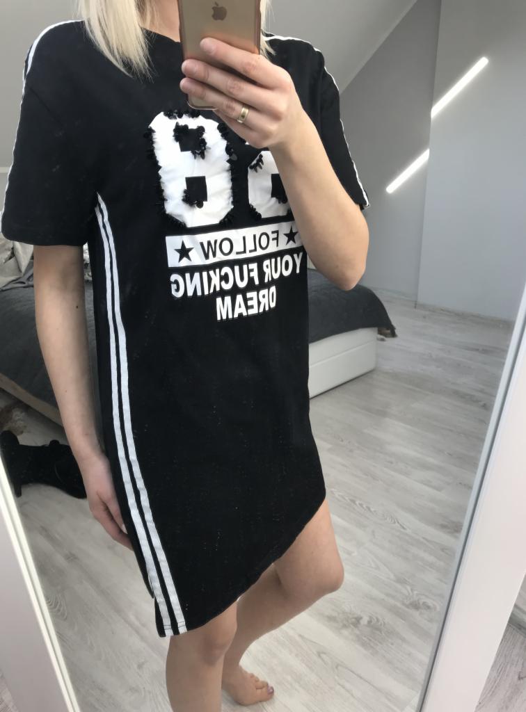 Osoba robi selfie w lustrze, prezentując czarną sukienkę/tunikę sportową z białymi paskami po bokach i napisem 'FOLLOW YOUR FUCKING DREAM' na przodzie.