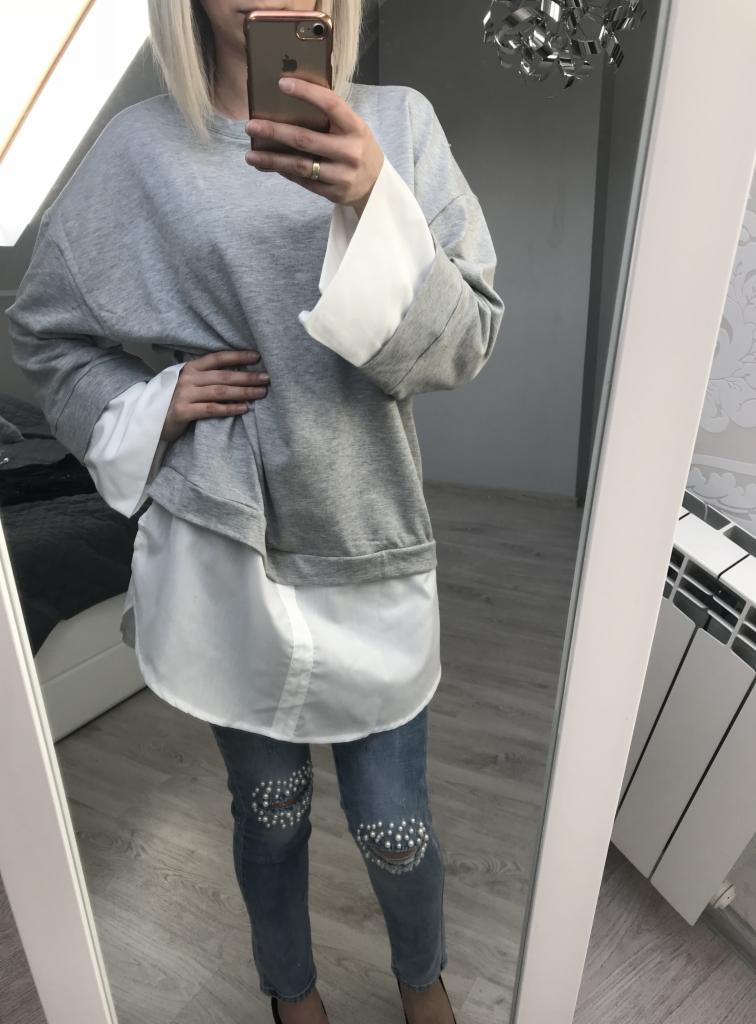 Selfie w lustrze prezentujące szarą bluzę z białymi mankietami i dżinsy z aplikacjami z perełek na kolanach.