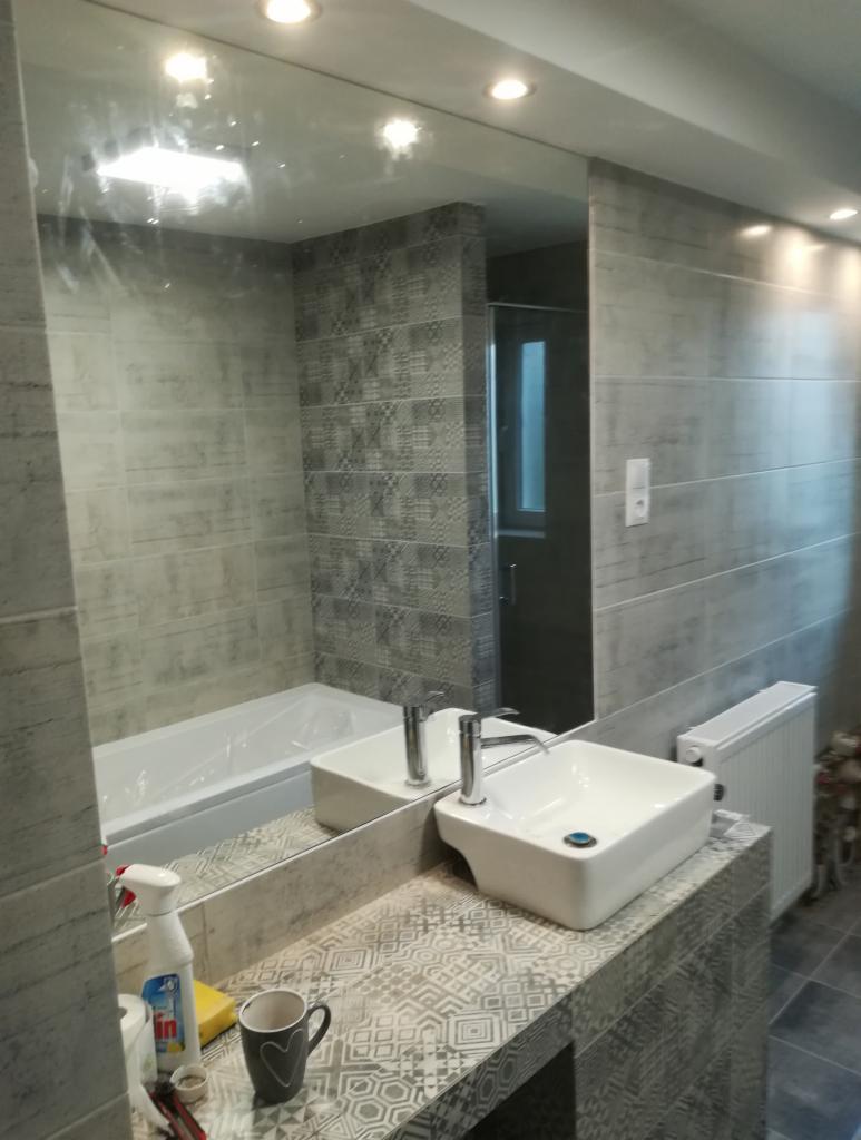 Nowoczesna łazienka w odcieniach szarości z prostokątną umywalką nablatową, baterią oraz dużym lustrem, widoczne płytki z wzorem geometrycznym i wanna.