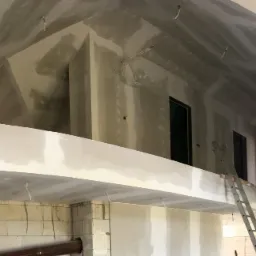 Wnętrze w trakcie prac wykończeniowych: ściany z płyt gipsowo-kartonowych, częściowo zaszpachlowane, aluminiowa drabina oparta o antresolę, widoczne instalacje elektryczne.