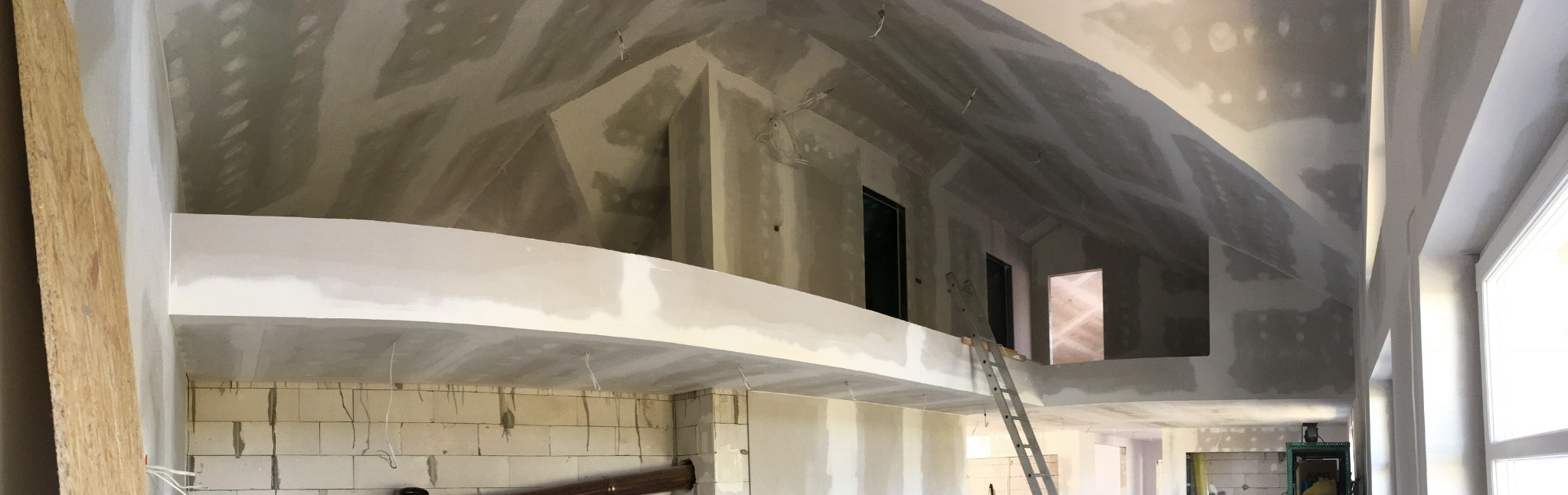 Wnętrze w trakcie prac wykończeniowych: ściany z płyt gipsowo-kartonowych, częściowo zaszpachlowane, aluminiowa drabina oparta o antresolę, widoczne instalacje elektryczne.