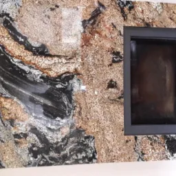 Kamienny blat z otworem na zlew, o unikalnym wzorze w odcieniach czerni, brązu i bieli, zamontowany w łazience w Lublinie, oświetlony punktowymi lampami.