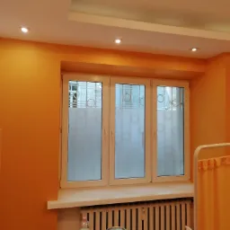 Pomarańczowe ściany w biurze z oknem z naklejoną folią z logo firmy, widoczny fragment wyposażenia medycznego