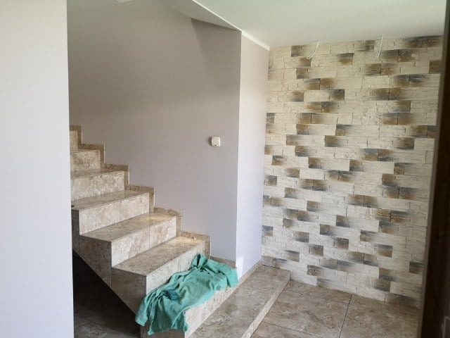 Klatka schodowa po remoncie: marmurowe schody, ściana z dekoracyjnej cegły, pomalowana na szaro ściana. Na schodach leży zielony ręcznik.