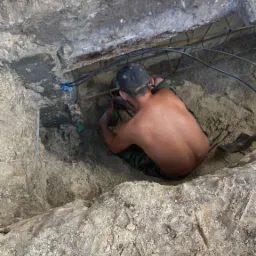 Pracownik w wykopie fundamentowym w Chorzowie, montuje zbrojenie; widoczne przewody i narzędzia.