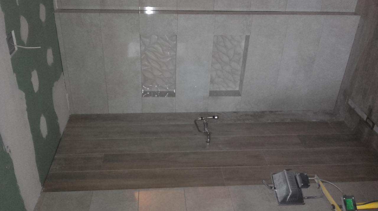 Wykończenie podłogi w łazience z użyciem płytek imitujących drewno, widoczne narzędzia glazurnicze i fragment ściany z dekoracyjnymi płytkami.