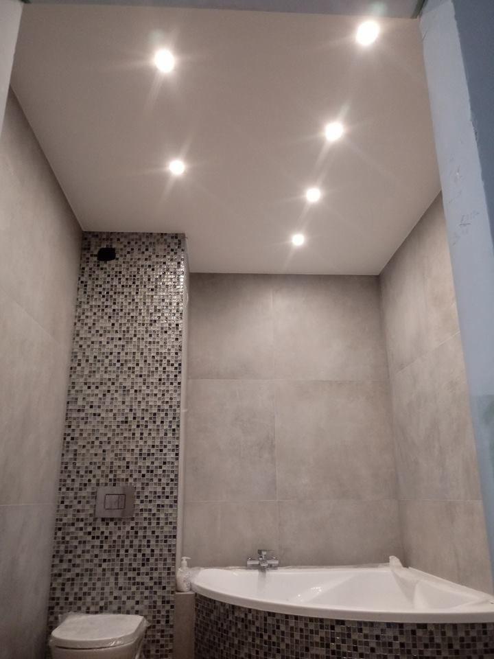 Wykończona łazienka z mozaiką przy zabudowie WC i w obudowie wanny narożnej, podwieszany sufit z sześcioma punktami świetlnymi.