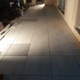 Układanie szarych płytek podłogowych z krzyżykami dystansowymi w Mroczkowej, widoczni pracownicy w tle.