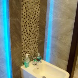 Nowoczesna łazienka z podświetlaną bidetką, mozaiką i marmurowymi płytkami ściennymi, uzupełniona o dozownik mydła i płyn do płukania ust.