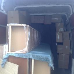 Mika Transport Przeprowadzki - Wnętrze furgonetki załadowanej kartonami i meblami, zabezpieczonymi folią i tkaniną, gotowymi do transportu podczas przeprowadzki.