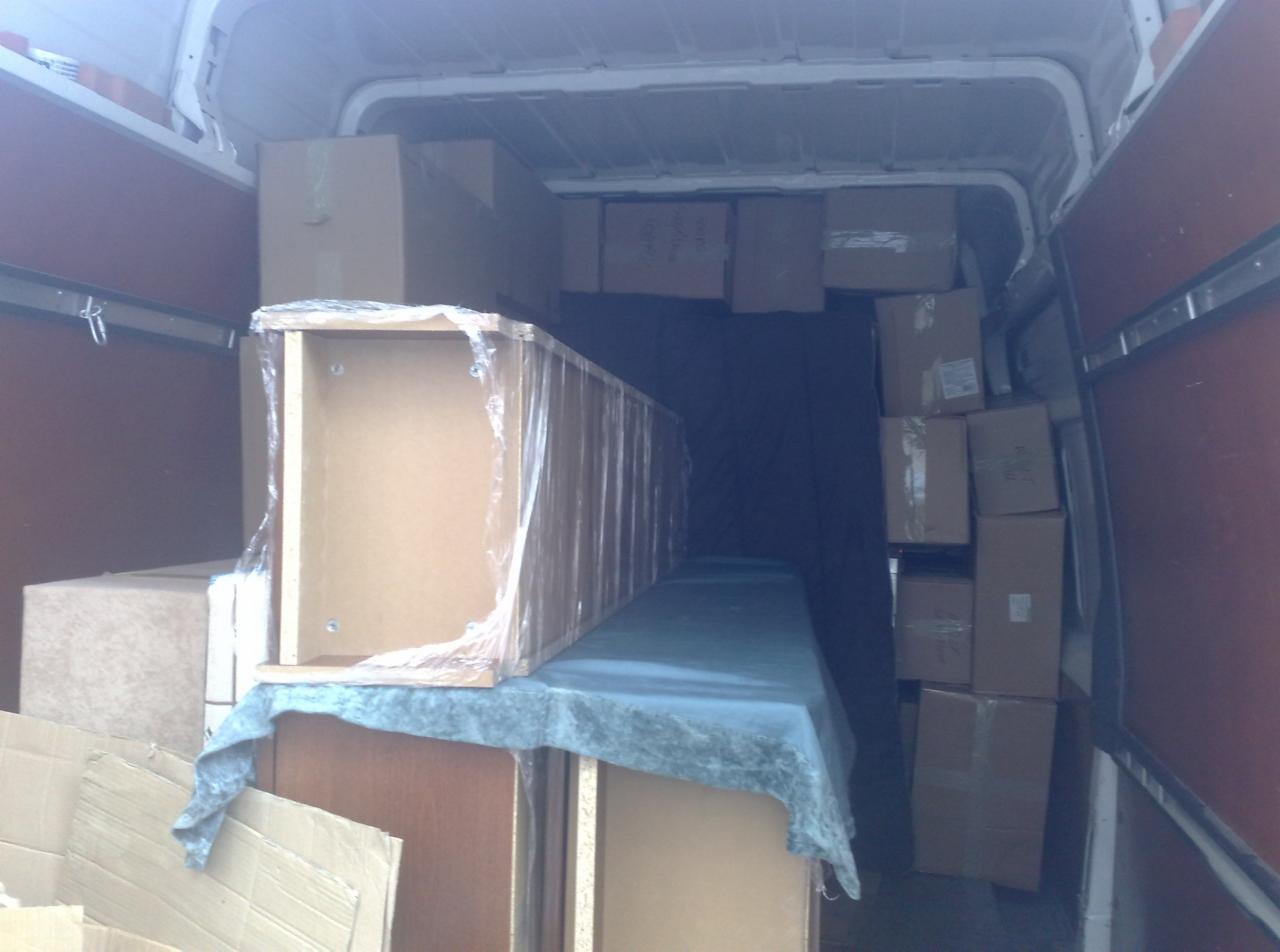 Wnętrze furgonetki załadowanej kartonami i meblami, zabezpieczonymi folią i tkaniną, gotowymi do transportu podczas przeprowadzki.