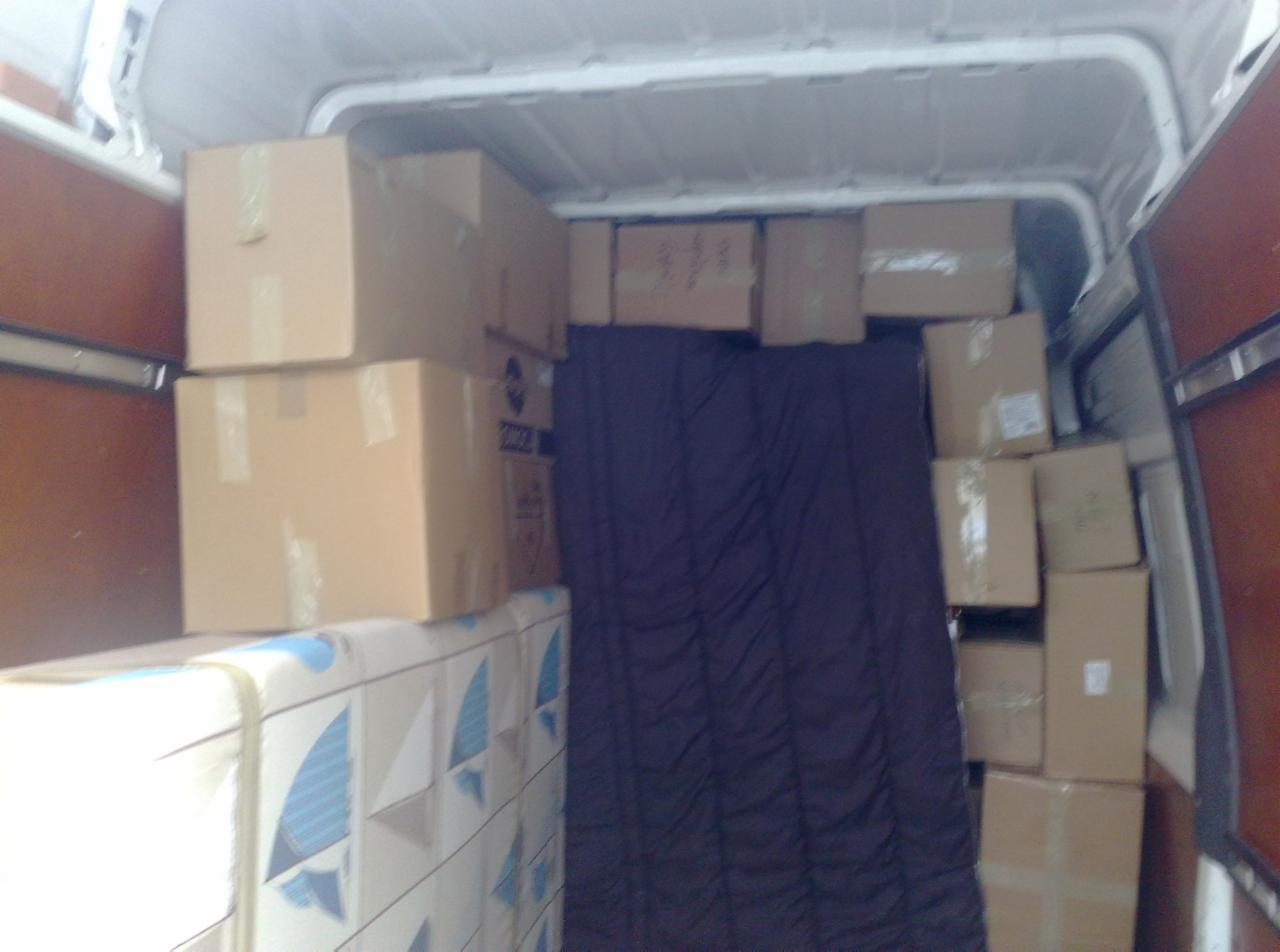 Wnętrze furgonetki wypełnionej kartonami i materacem zabezpieczonym folią, gotowe do transportu.