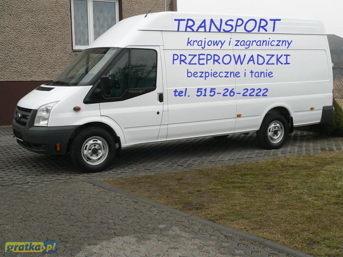 Biały samochód dostawczy z niebieskim napisem 'TRANSPORT krajowy i zagraniczny' oraz 'Przeprowadzki bezpieczne i tanie' i numerem telefonu, zaparkowany na kostce brukowej.