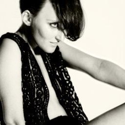 Jakubowska FOTO - Portret kobiety w czarno-białej tonacji, ubrana w koronkową kamizelkę, z włosami opadającymi na jedno oko, spoglądająca w dół.