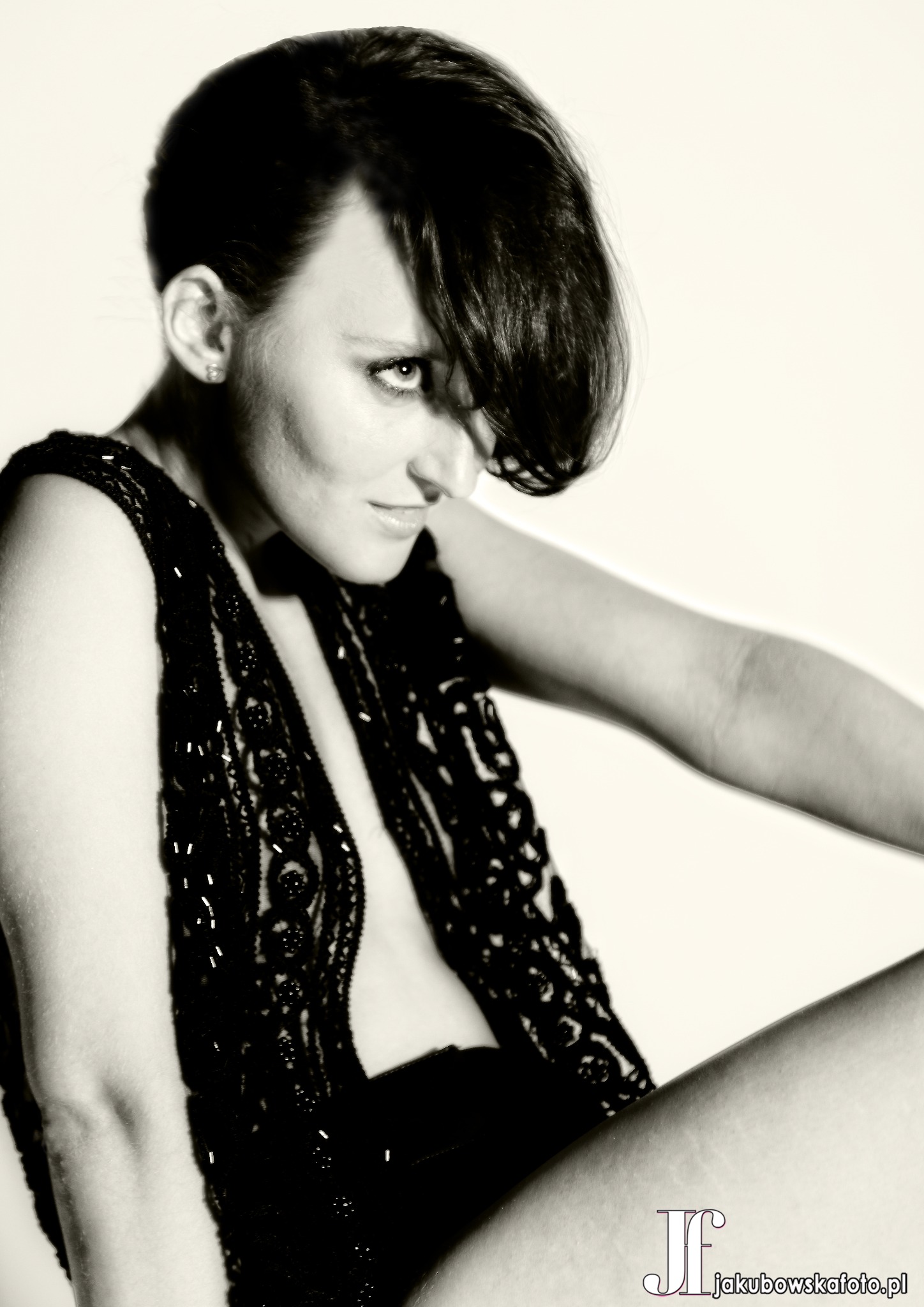 Portret kobiety w czarno-białej tonacji, ubrana w koronkową kamizelkę, z włosami opadającymi na jedno oko, spoglądająca w dół.