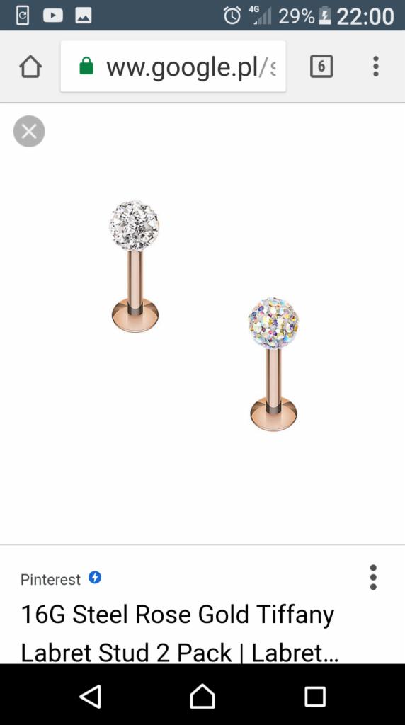 Dwa kolczyki labret w kolorze różowego złota z kryształową kulką, jeden z przezroczystymi kryształkami, drugi z opalizującymi, na białym tle.