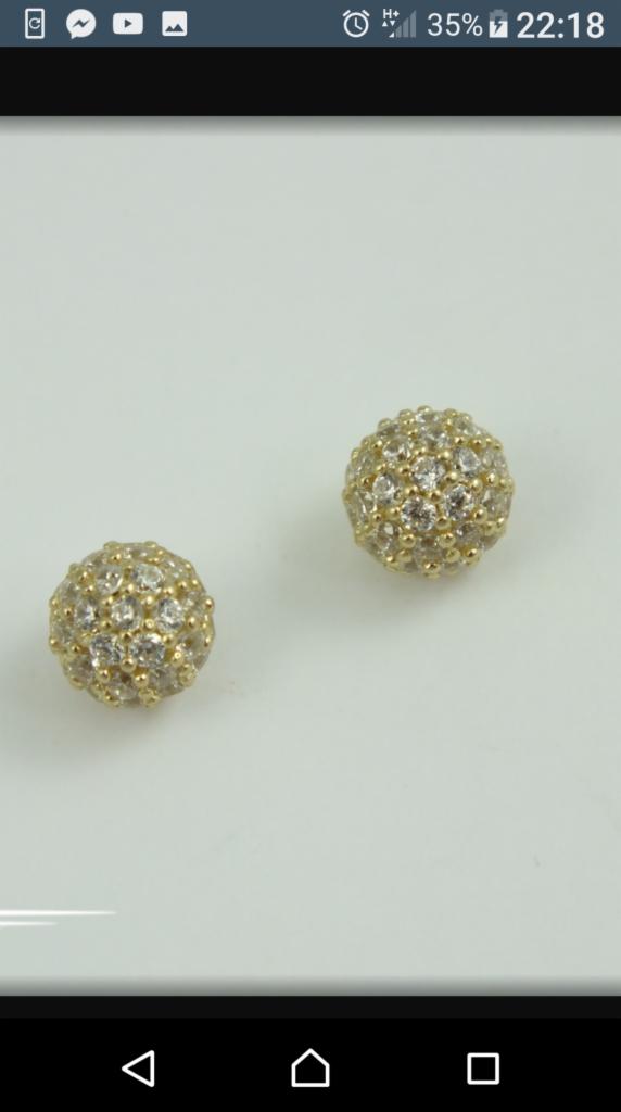 Dwie złote kulki kolczyków wysadzane drobnymi kryształkami na białym tle, zbliżenie.