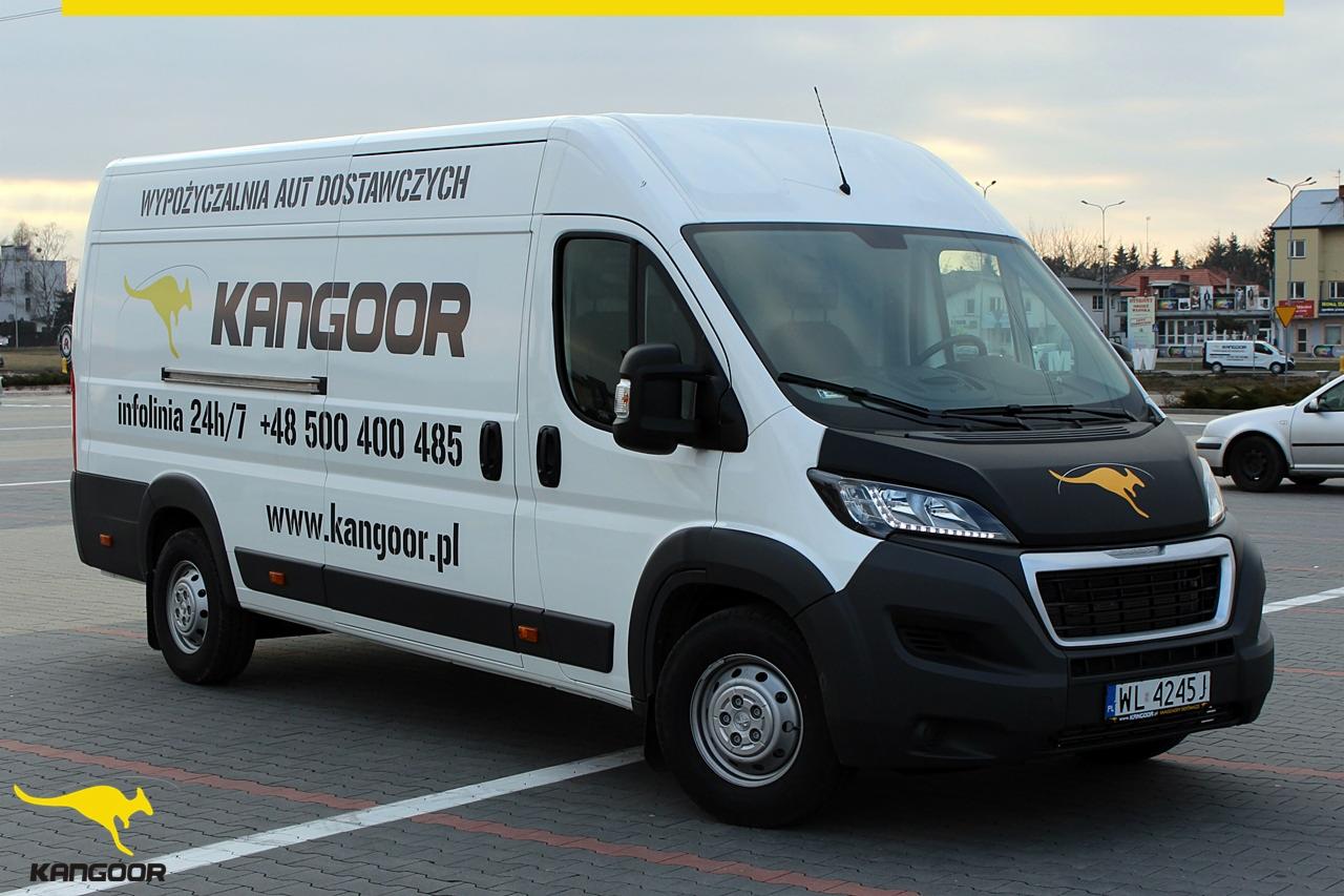 Biały bus dostawczy z logo Kangooor na parkingu, widoczne dane kontaktowe i adres strony internetowej na karoserii.