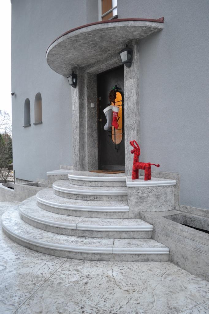 Zewnętrzne schody półokrągłe z szarego betonu architektonicznego prowadzące do wejścia domu, udekorowane świątecznym wieńcem i skarpetami, z czerwoną dekoracją renifera na jednym z stopni.