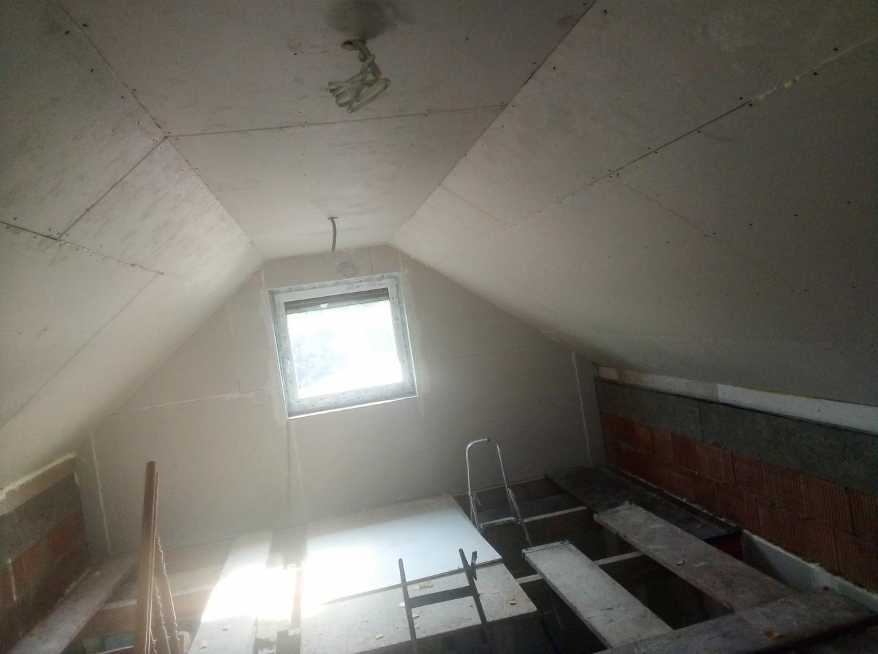 Poddasze po montażu płyt karton-gips z oknem dachowym i widoczną konstrukcją podłogi. Widoczne łączenia płyt na suficie i ścianach.