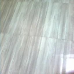 Jasne, błyszczące panele podłogowe z delikatnym wzorem drewna, ułożone w regularny wzór, z widocznym odbiciem światła w dolnym rogu.