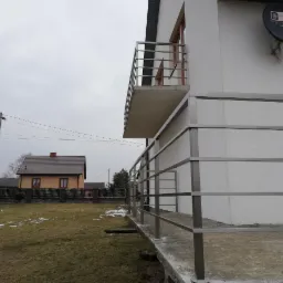 Metalowa balustrada na tarasie i balkonie domu jednorodzinnego w pochmurny dzień, widoczne elementy montażowe.