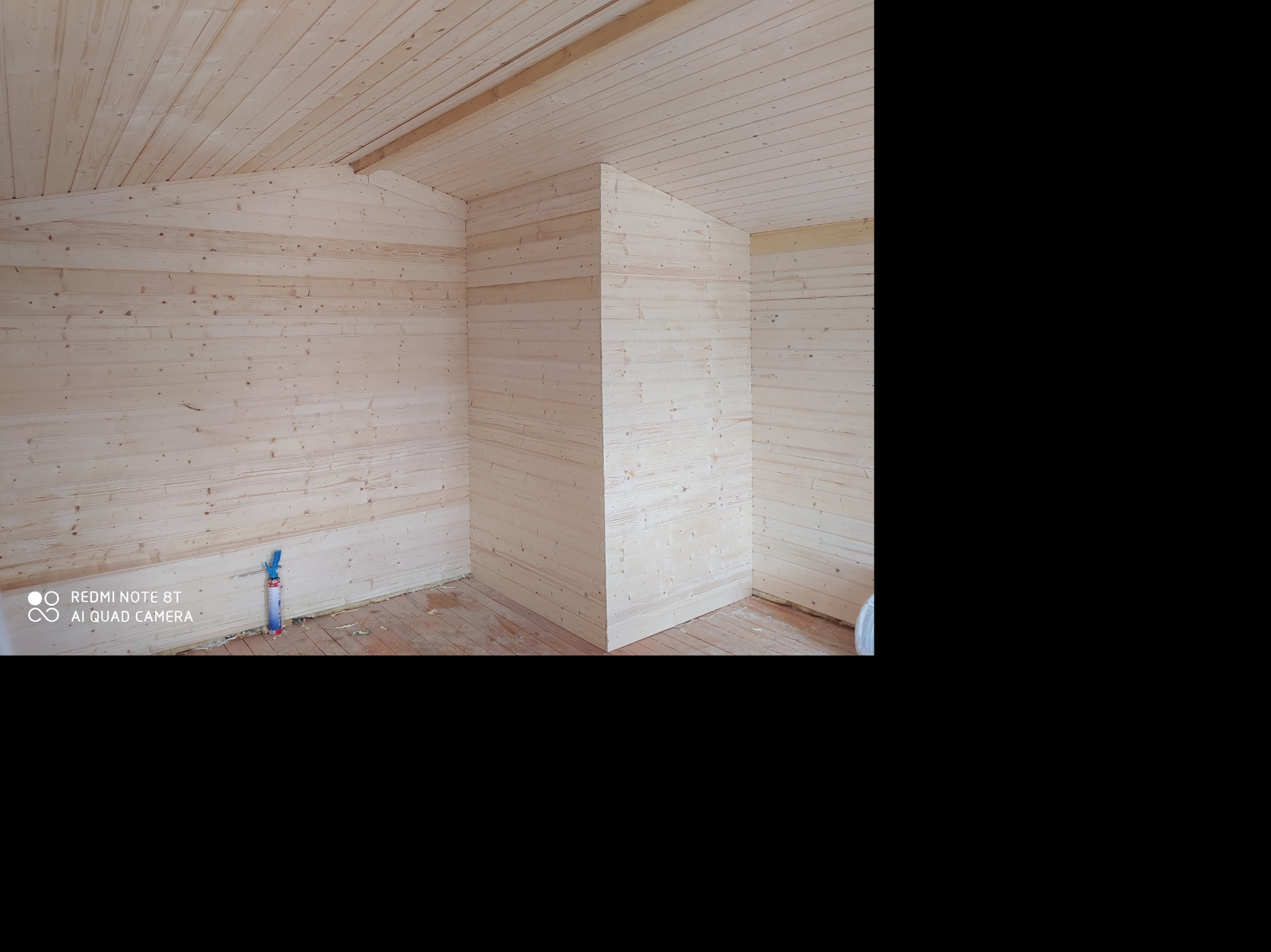 Wnętrze w trakcie budowy lub wykończenia, ściany i sufit wyłożone jasnym drewnem, widoczna puszka z pianką montażową przy ścianie.