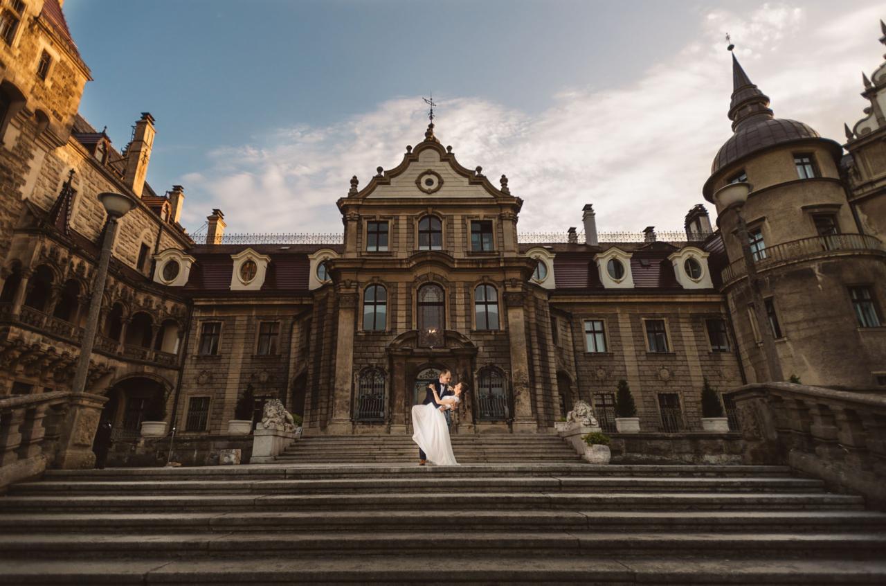 Para młoda tańczy na schodach monumentalnego zamku w Mosznej, Polska, w promieniach zachodzącego słońca.