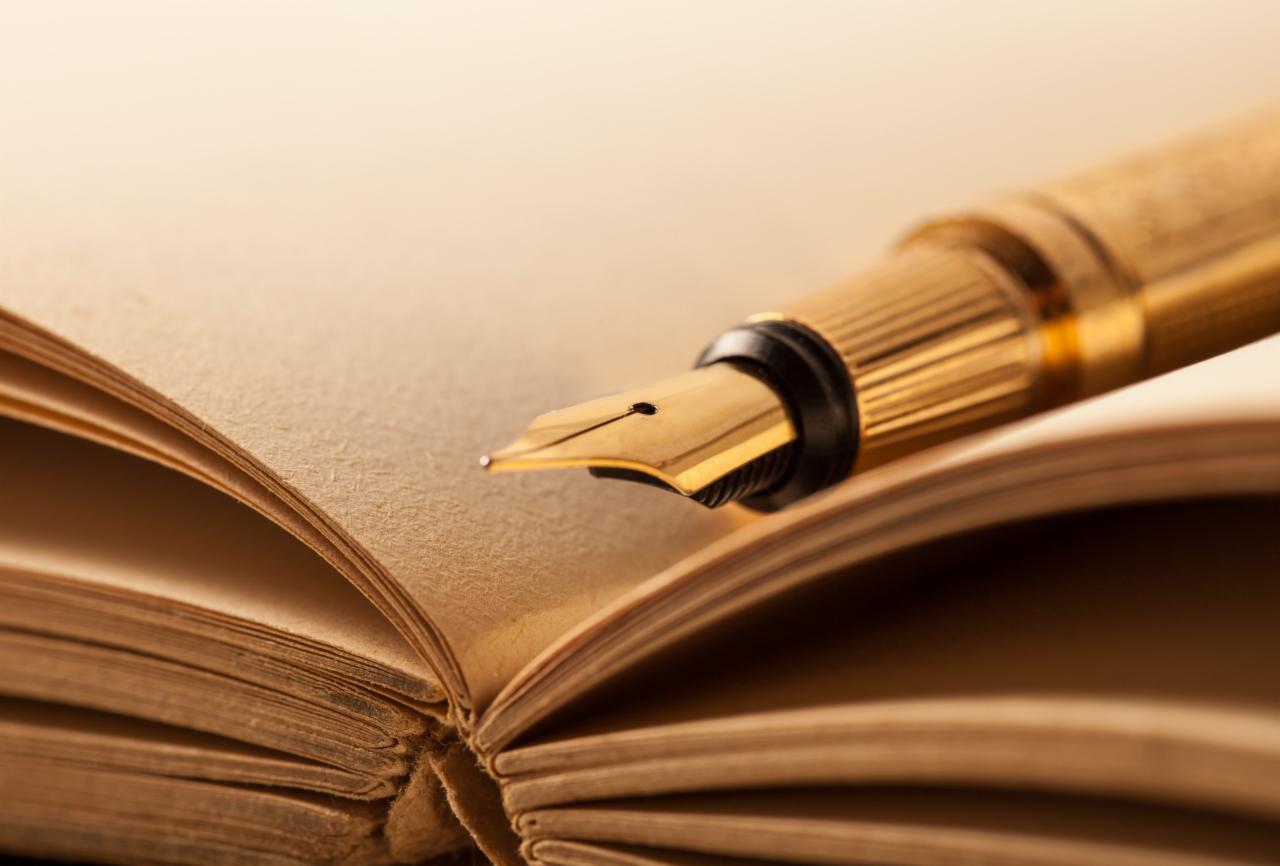 Złote pióro wieczne spoczywające na otwartej, starej książce z pożółkłymi stronami, ukazane w ciepłym oświetleniu.