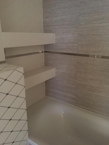 Wykończona łazienka z półkami wnękowymi, szare płytki imitujące drewno na ścianie i geometryczny wzór płytek na obudowie wanny.