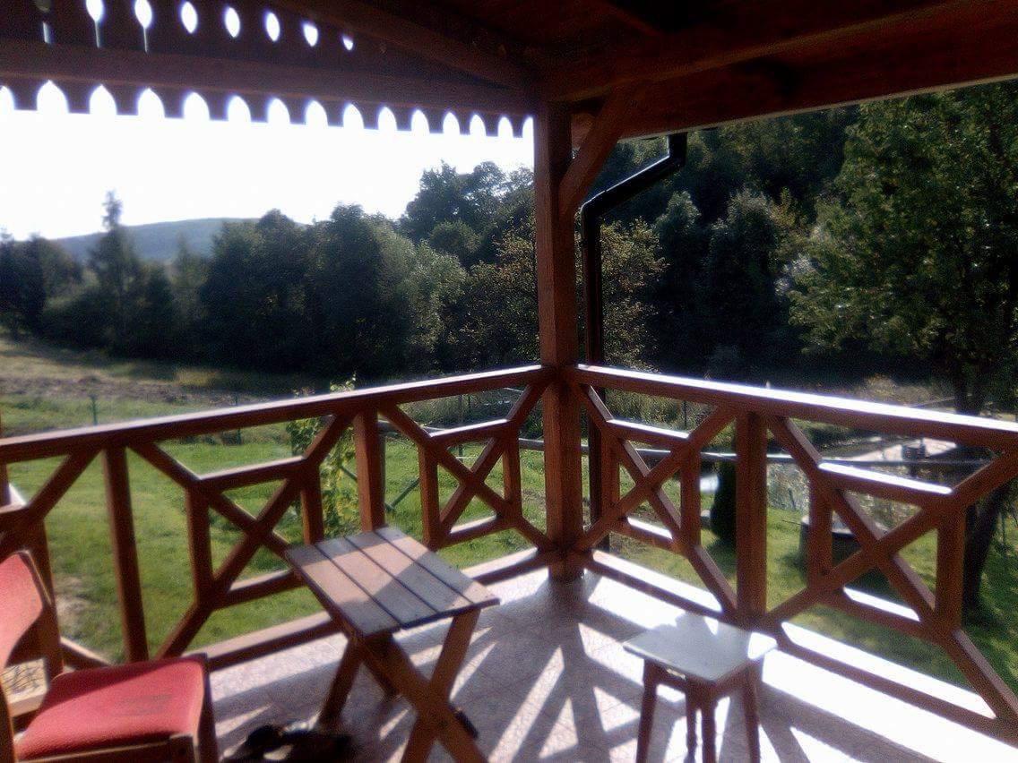 Drewniana balustrada balkonu z widokiem na zalesione wzgórze, mały stolik i krzesło na słonecznym balkonie.