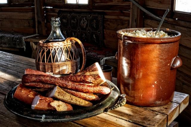 Tradycyjny stół z wędlinami na srebrnej tacy, butelką wina w wiklinowym koszu i garnkiem kapusty kiszonej w rustykalnej chacie.