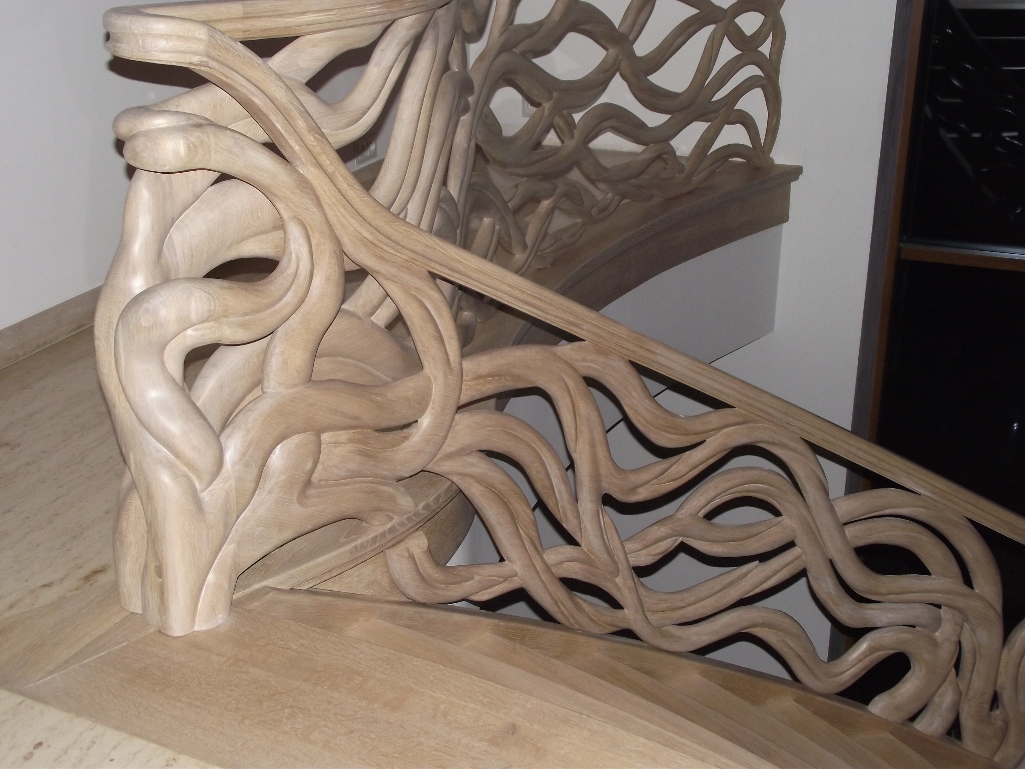 Rzeźbiona balustrada z jasnego drewna w kształcie fal, zdobiąca schody z drewnianymi stopniami.