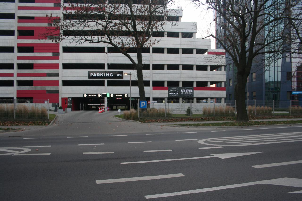 Wjazd do wielopoziomowego parkingu z reklamą auto myjni na elewacji budynku.