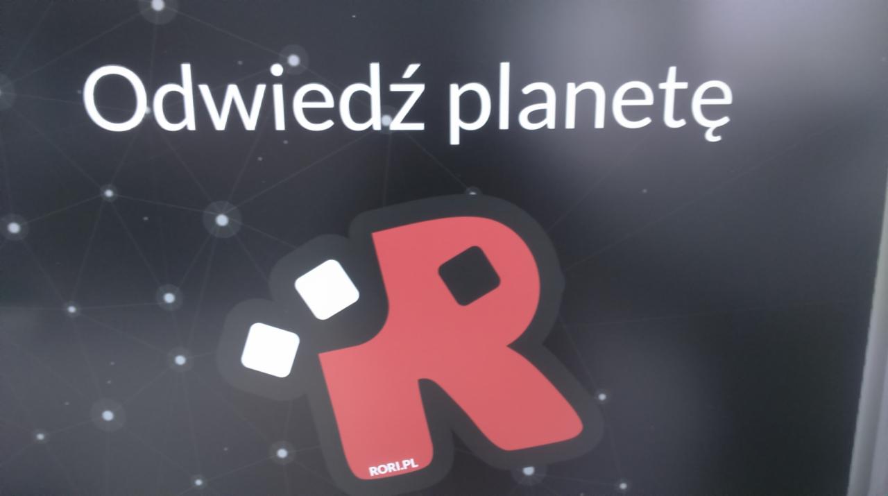 Ekran z napisem 'Odwiedź planetę' i czerwonym logo litery R z dwoma białymi kwadratami na tle kosmicznej siatki połączeń.