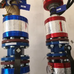 Dwa izolowane zawory odcinające, jeden niebieski z zaworem skośnym i etykietą '19', drugi czerwony z manometrem i strzałką, oba z widocznymi etykietami 'K.Z.' i oznaczeniami 'ZAWÓR ODCINAJĄCY'.