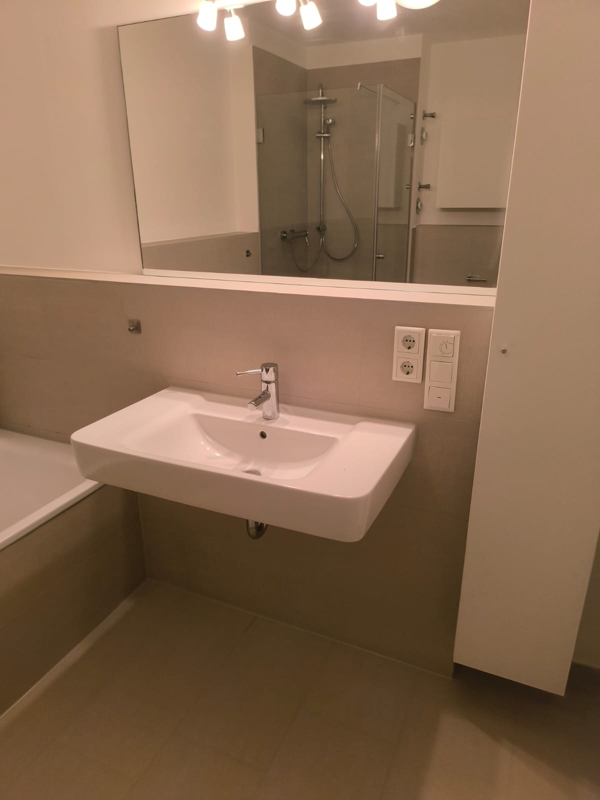 Nowoczesna łazienka po remoncie: biała umywalka nablatowa z chromowaną baterią, duże lustro z widokiem na kabinę prysznicową i beżowe płytki.