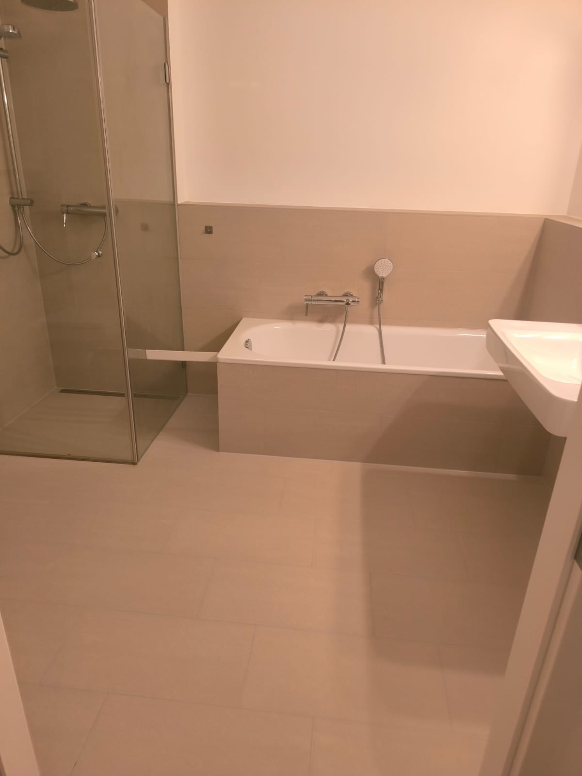 Beżowa łazienka po remoncie: kabina prysznicowa, wanna z baterią i umywalka. Stonowana kolorystyka, płytki podłogowe i ścienne. Minimalistyczny design.