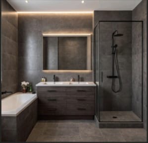 Nowoczesna łazienka w szarościach: płytki imitujące kamień, podświetlane lustro nad podwójną umywalką, kabina prysznicowa typu walk-in i wanna.
