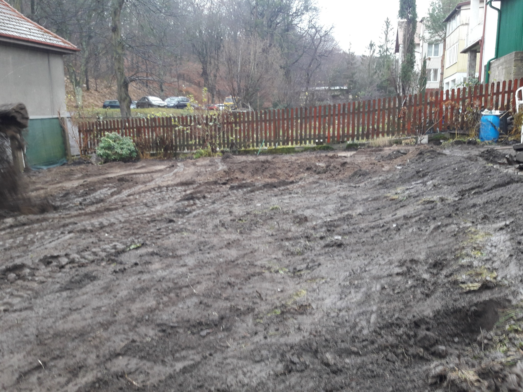 Przygotowany teren pod trawnik po przekopaniu, widoczne ślady opon i resztki darni, w tle drewniany płot i zabudowania.