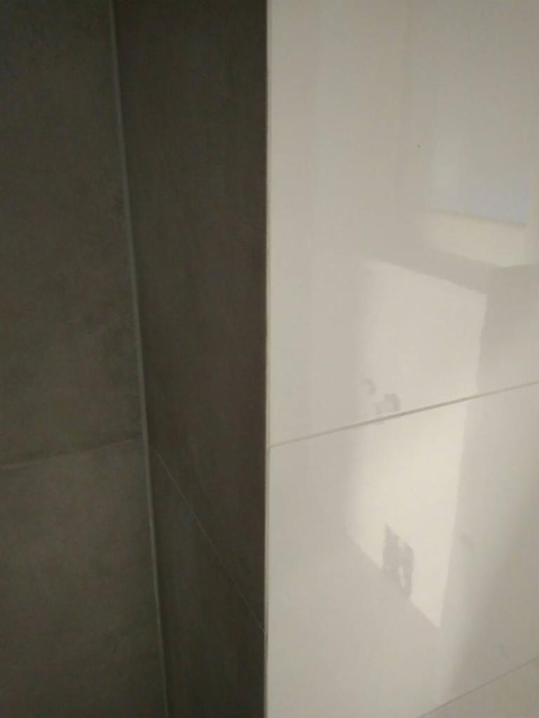 Styk szarej matowej i białej błyszczącej płytki ściennej, widoczne fugi i odbicia światła.