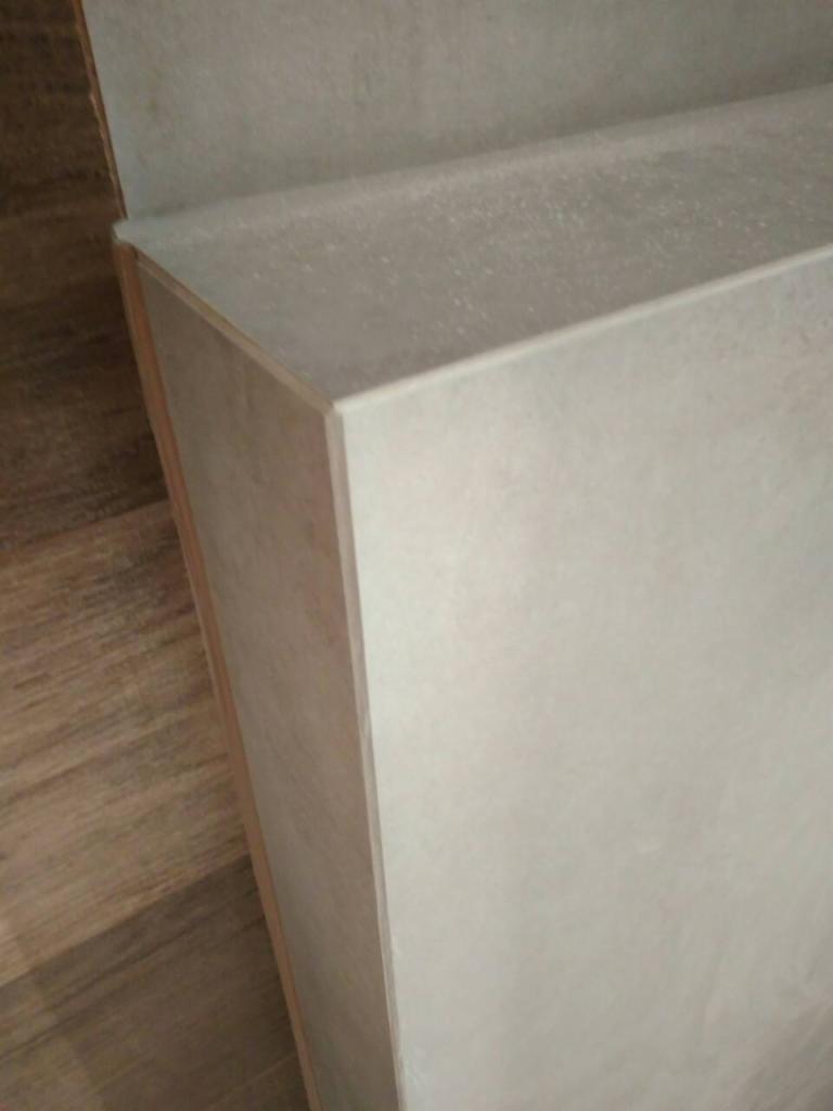 Szlifowana krawędź płyty kartonowo-gipsowej, widoczna struktura i gładkie wykończenie, podłoga z paneli w tle.