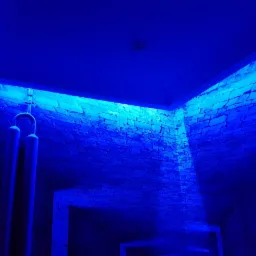 Ściana z kamienia dekoracyjnego oświetlona intensywnym niebieskim światłem LED, widoczne elementy instalacji wodnej.