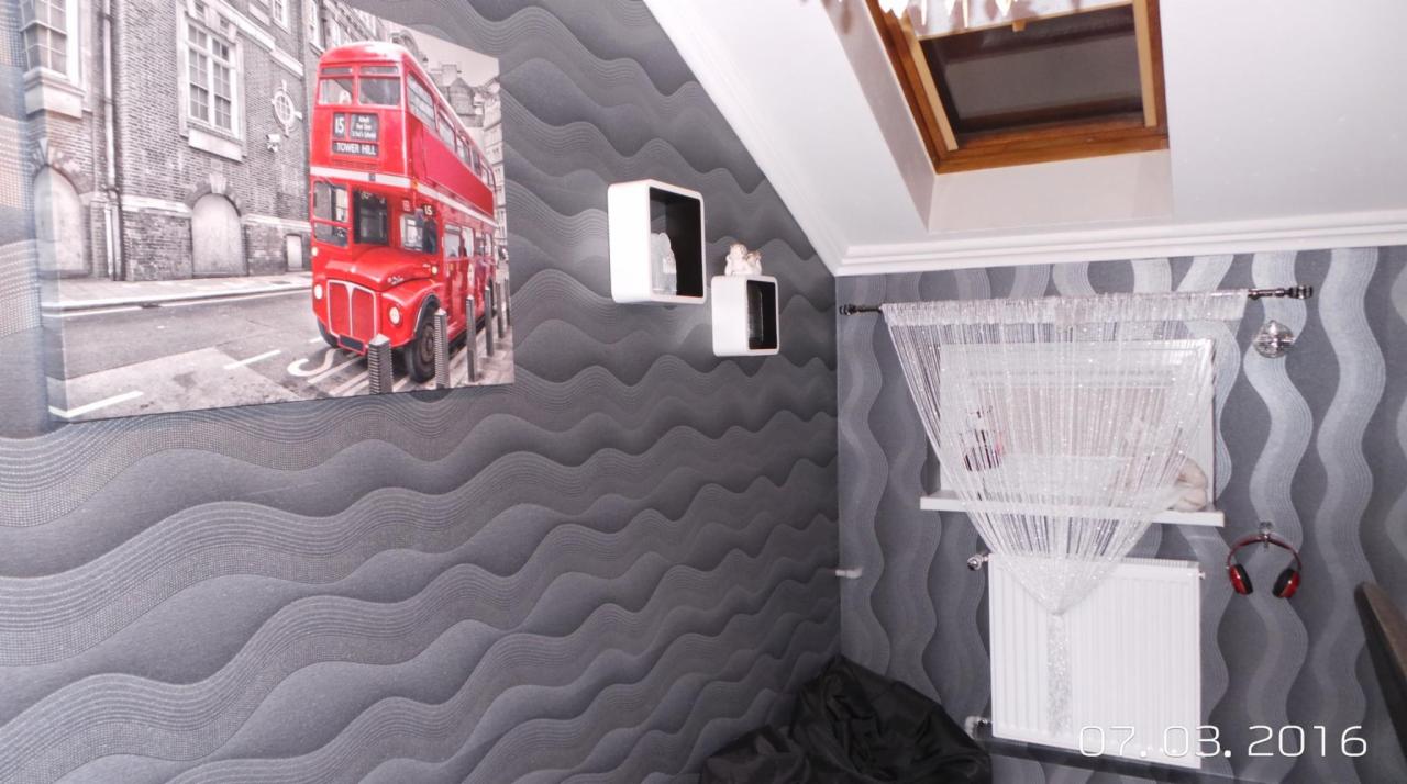 Pokój z szarą tapetą w fale, obrazem czerwonego autobusu, białymi półkami i dekoracyjną zasłoną z koralików.