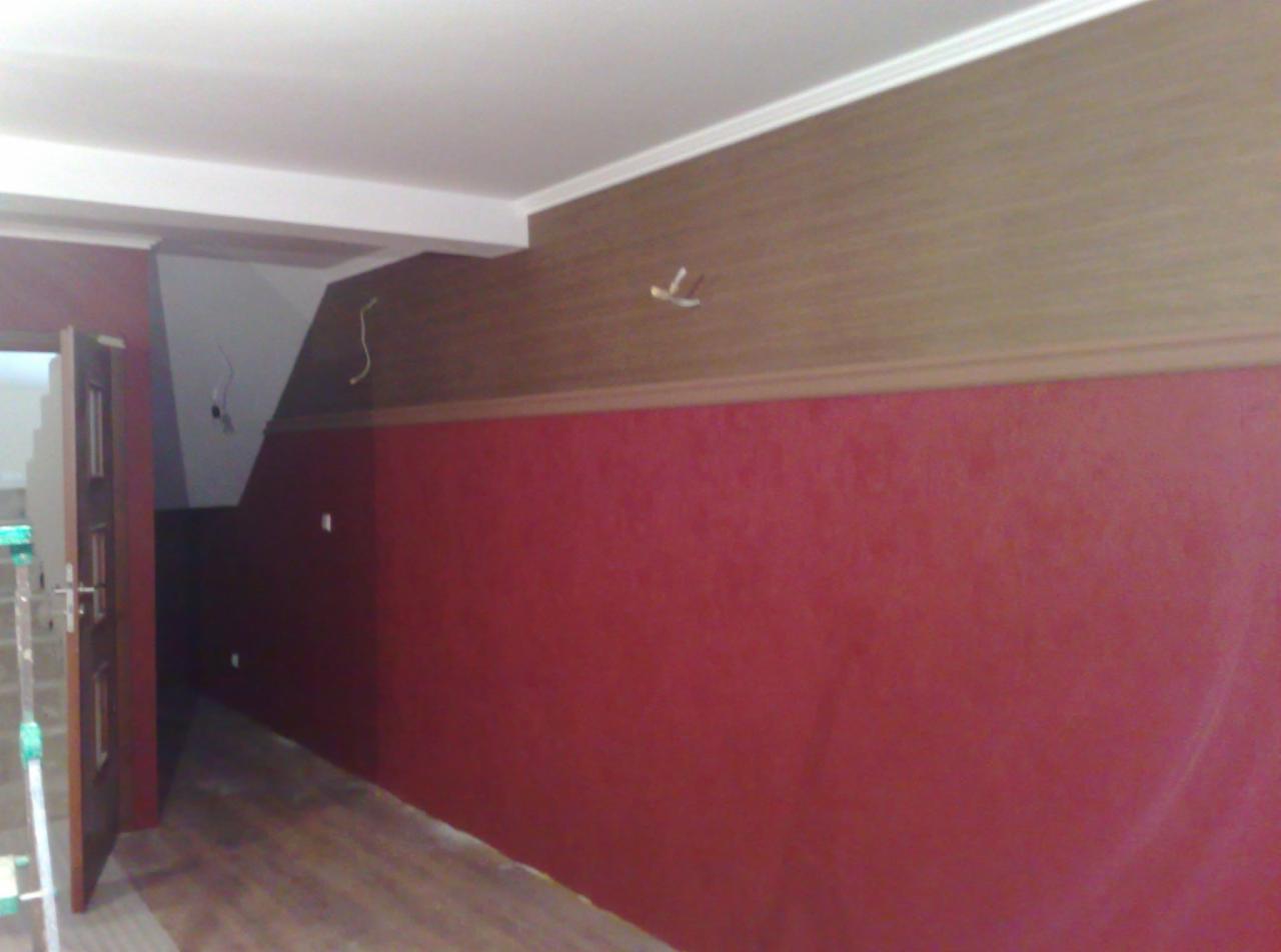 Pokój po remoncie z dwukolorowymi ścianami: dolna część w kolorze ciemnej czerwieni, górna w odcieniach brązu, widoczne wystające przewody elektryczne i częściowo otwarte drzwi.