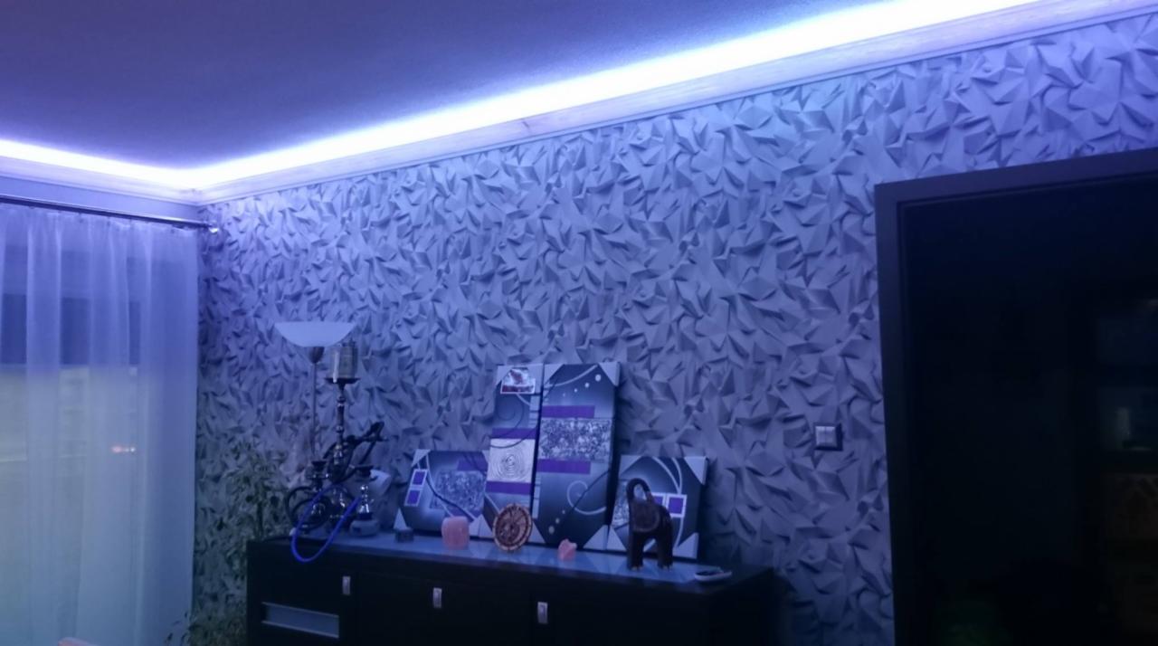 Pokój z trójwymiarową tapetą w odcieniach szarości, oświetlony listwą LED na suficie, z widoczną komodą i dekoracjami.