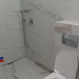 Nowoczesna łazienka z białymi płytkami imitującymi marmur, wisząca toaleta z otwartą klapą, chromowana bateria prysznicowa i odpływ liniowy.