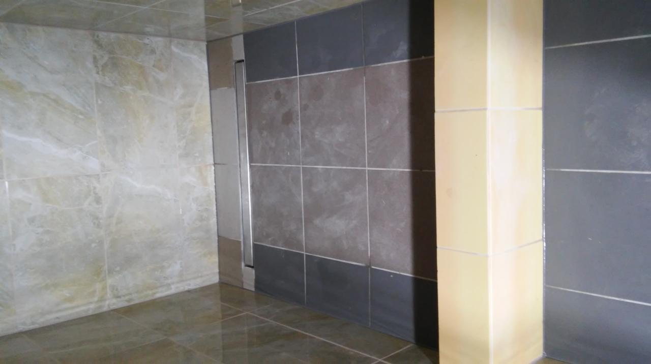 Wykończona łazienka z marmurowymi płytkami na ścianach i podłodze, kontrastująca z ciemnymi płytkami w strefie prysznicowej i jasną kolumną.