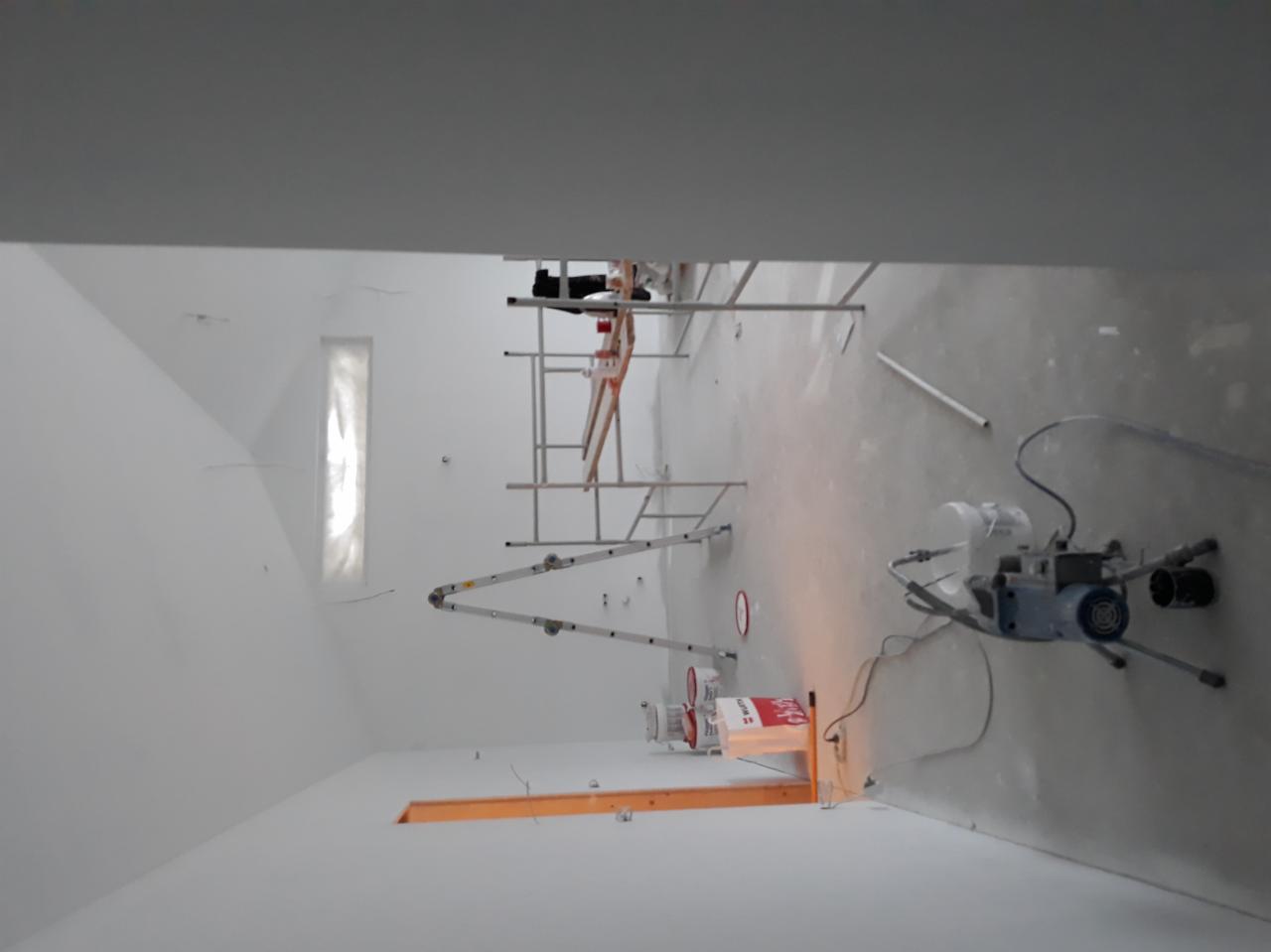 Wnętrze w trakcie prac wykończeniowych, widoczne rusztowania, drabina, agregat malarski i puszki z farbą Wurth przy otworze w ścianie.